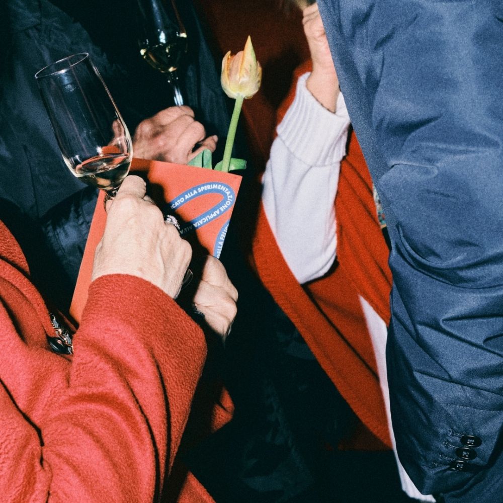 Clienti che parlano e hanno tra le mani la brochure dell'evento e calici di vino