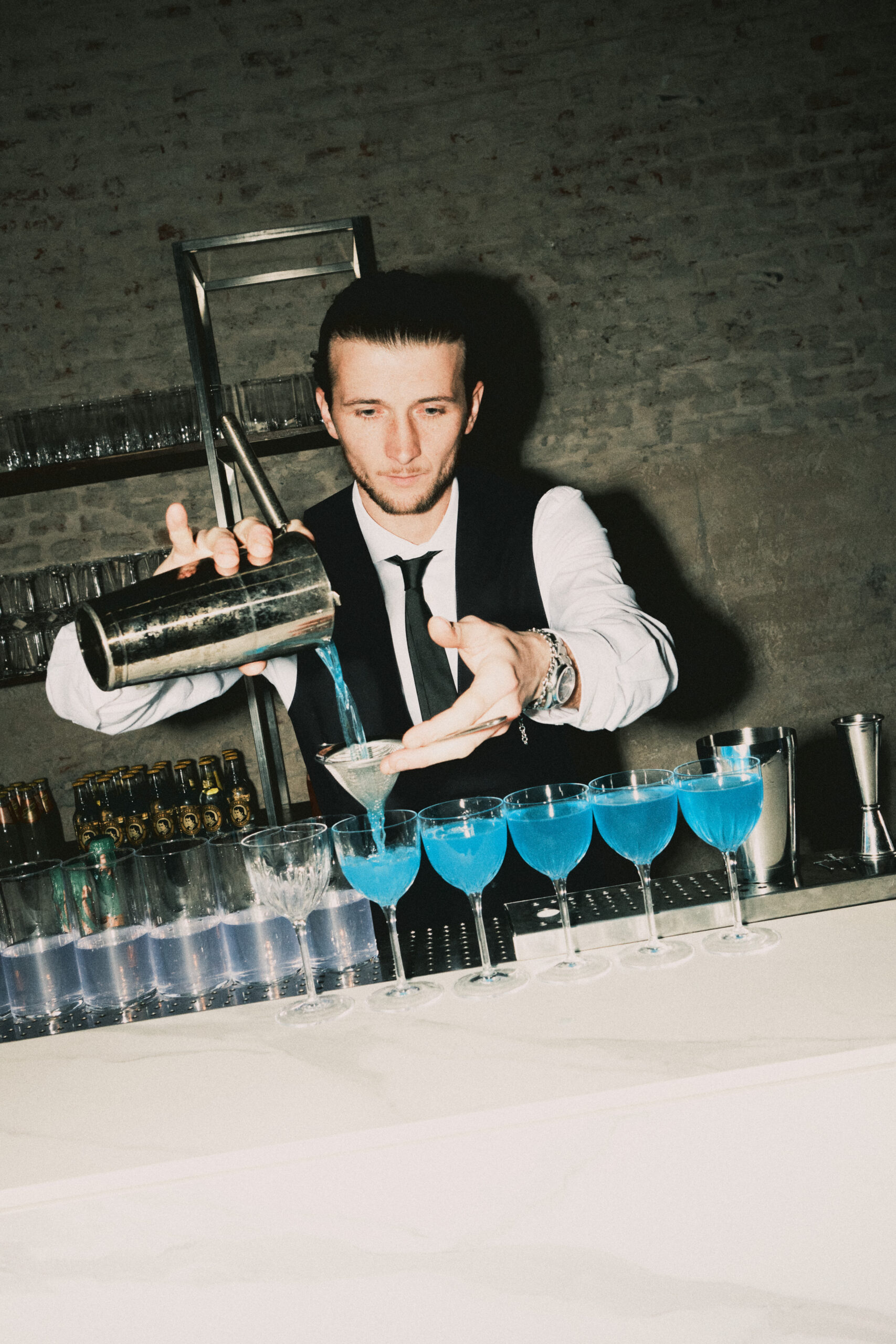 Barman che versa un drink azzurro nei bicchieri disposti in fila
