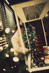 Cameriere prepara una fontana di cioccolato con fragole e marshmallow davanti a un albero di Natale illuminato